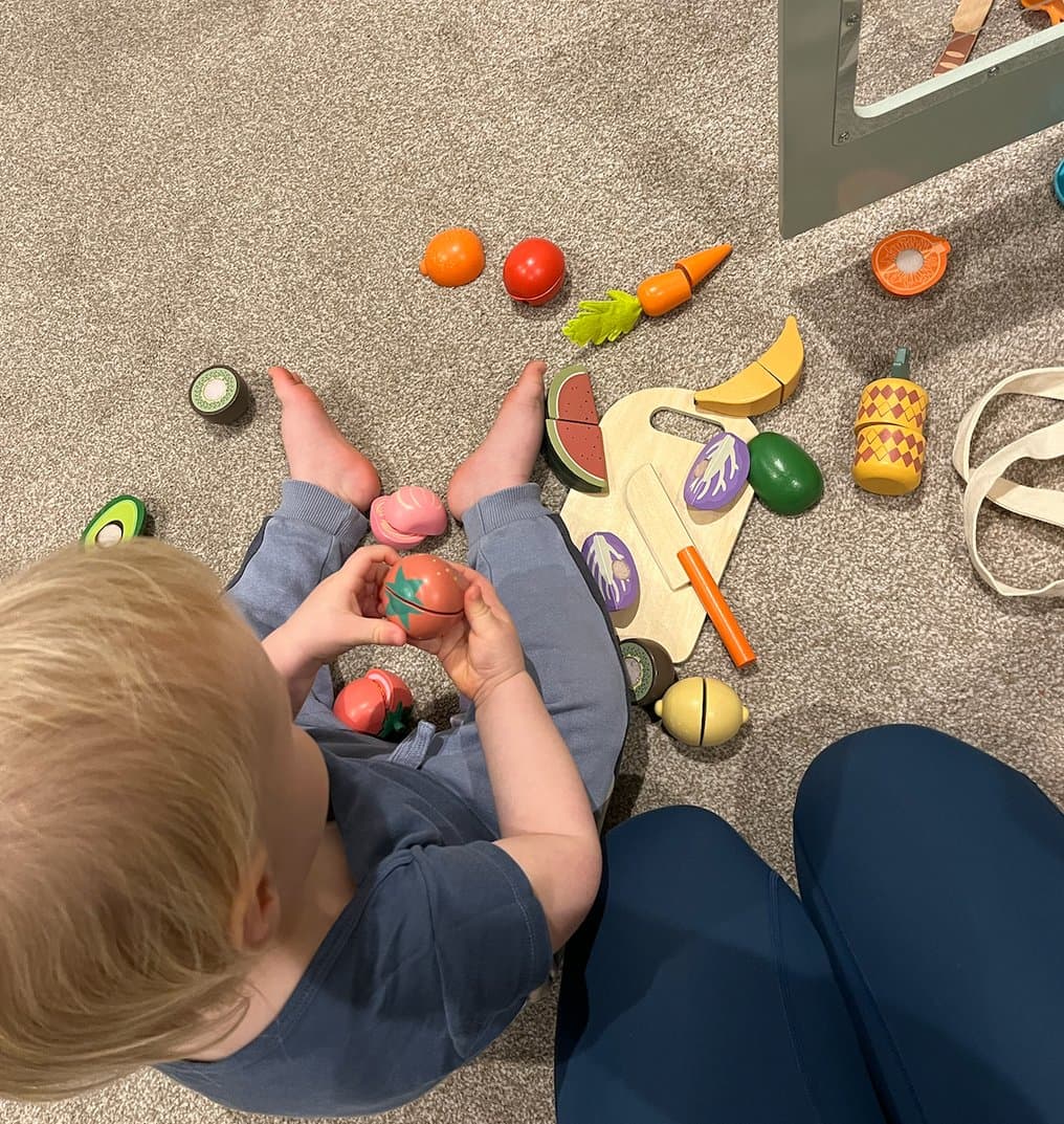 A toddler playing with wooden toy food